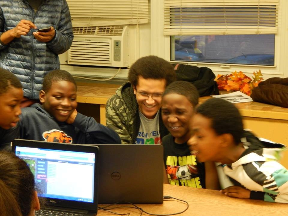 Young Adinkra students gathered around a laptop with a student teacher