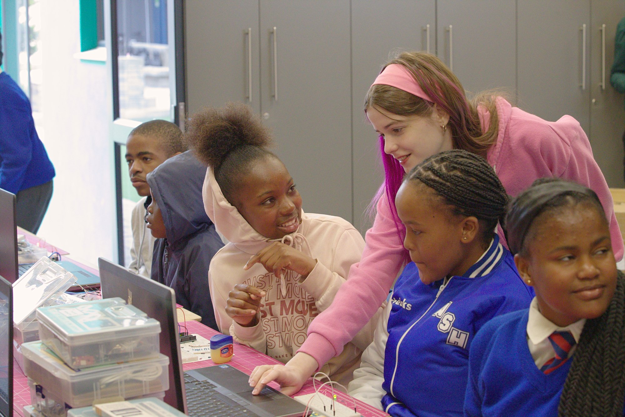 Cecilia Bilski, an ETHS student, leans in over a laptop with Namibian students, one of them turning back to smile at her
