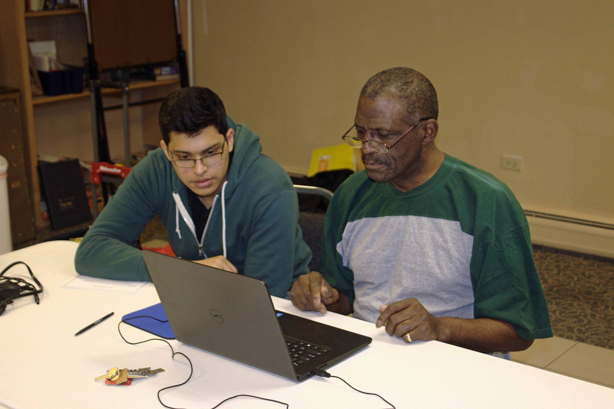 An ETHS YTC student in a green hoodie helps a Primm Towers resident with a laptop
